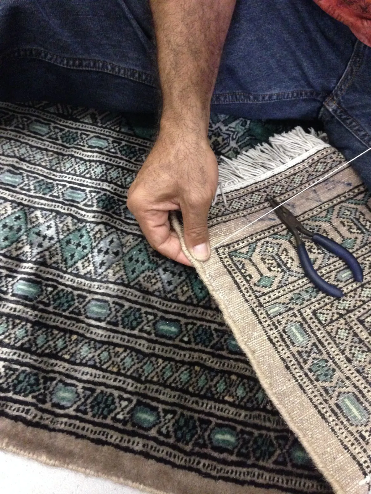 Close detail of a hand securing the worn fringe at the end of an oriental rug