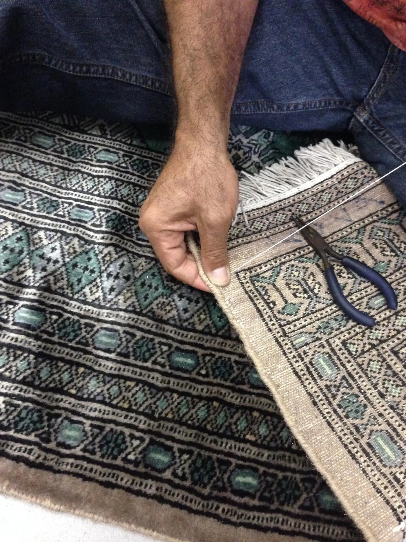A hand re-wrapping and overcasting the frayed side edge of a rug with matched yarn