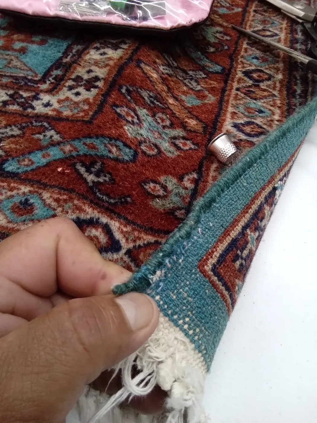 Hands rebuilding the red fringe at the end of a rug by hand