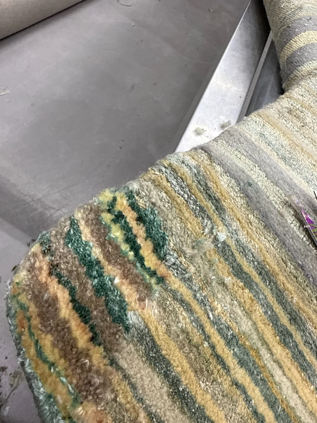 Worn area of a green rug showing pile loss, noted at inspection