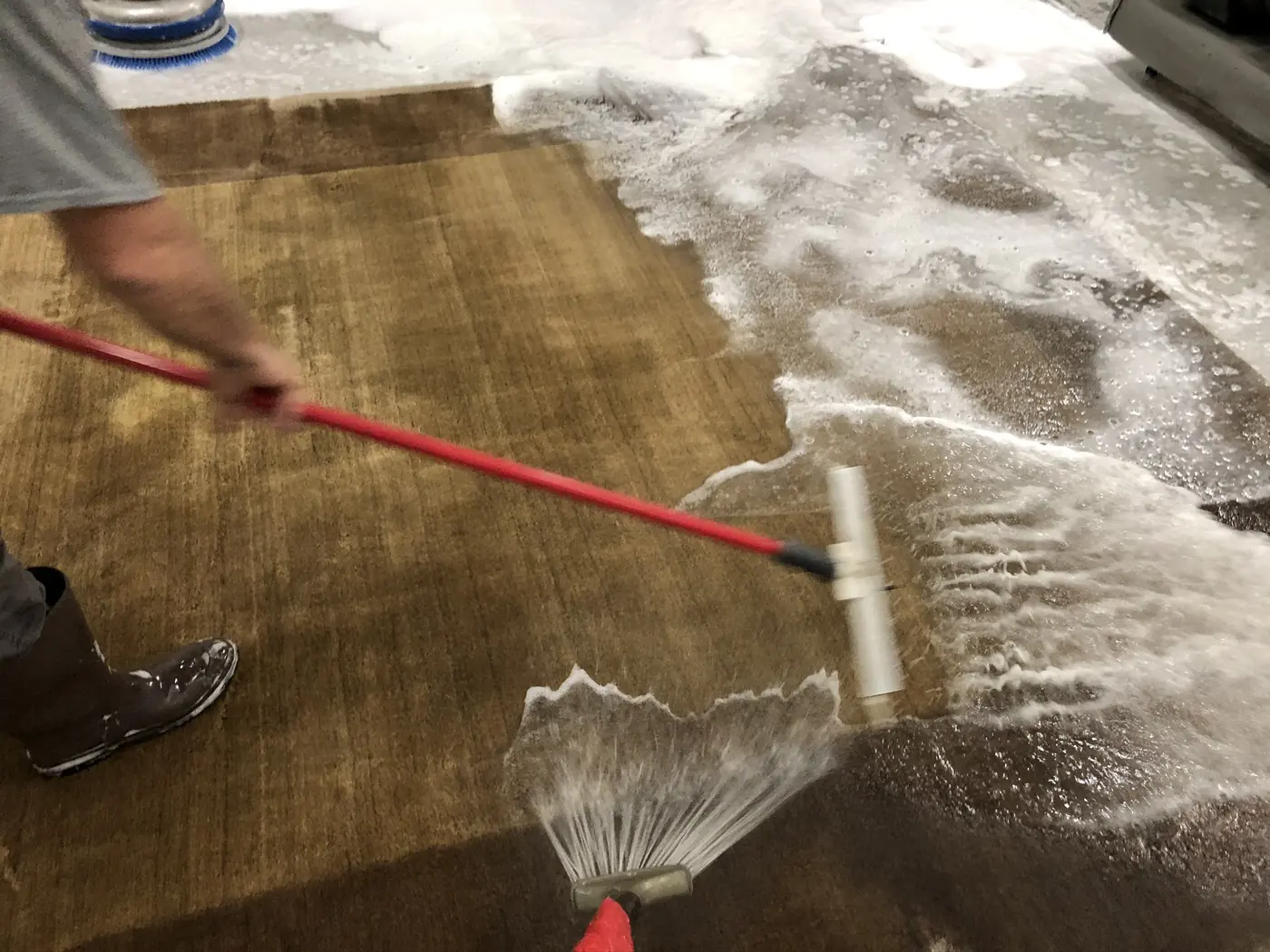 Rug being rinsed on the wash floor with a handheld rinse wand